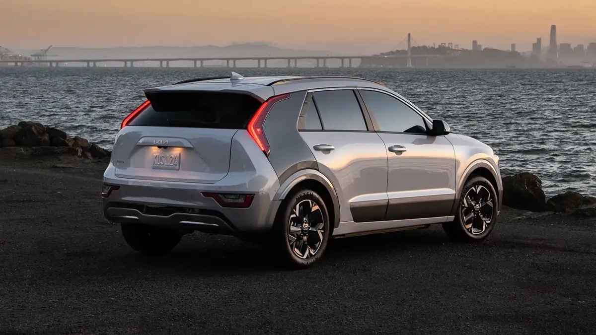 Kia Niro EV 2025 vu de l’arrière au coucher du soleil avec vue sur un pont en arrière-plan.
