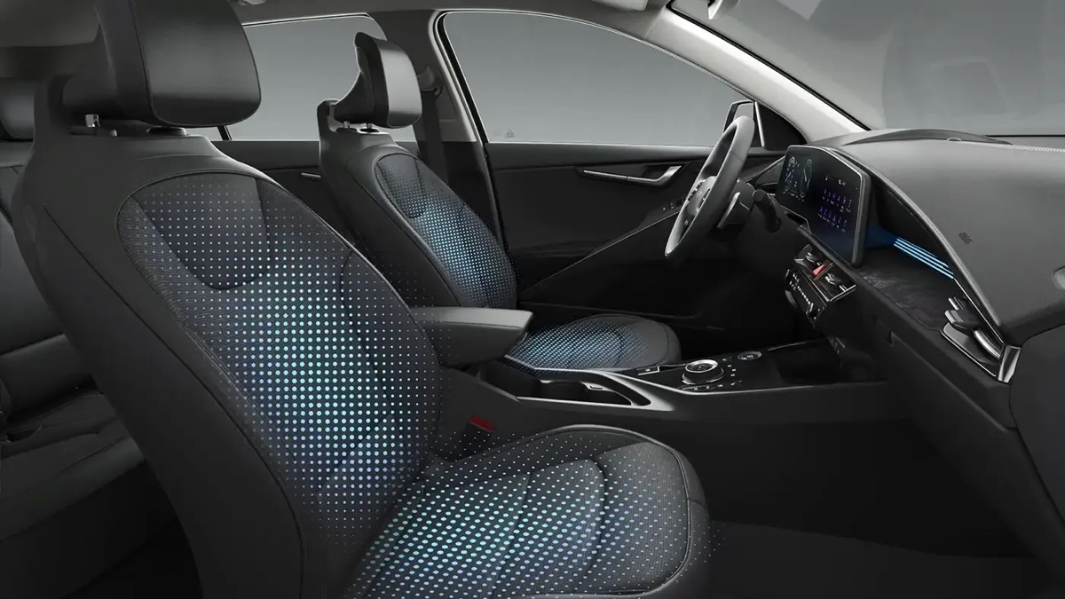 Habitacle avant du Kia Niro EV 2025 avec sièges en tissu perforé et tableau de bord numérique.